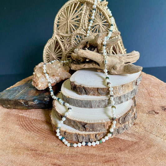 Decorative arrangement with wooden elements and a beaded  Pearl and Black Opal necklace on a dark blue background