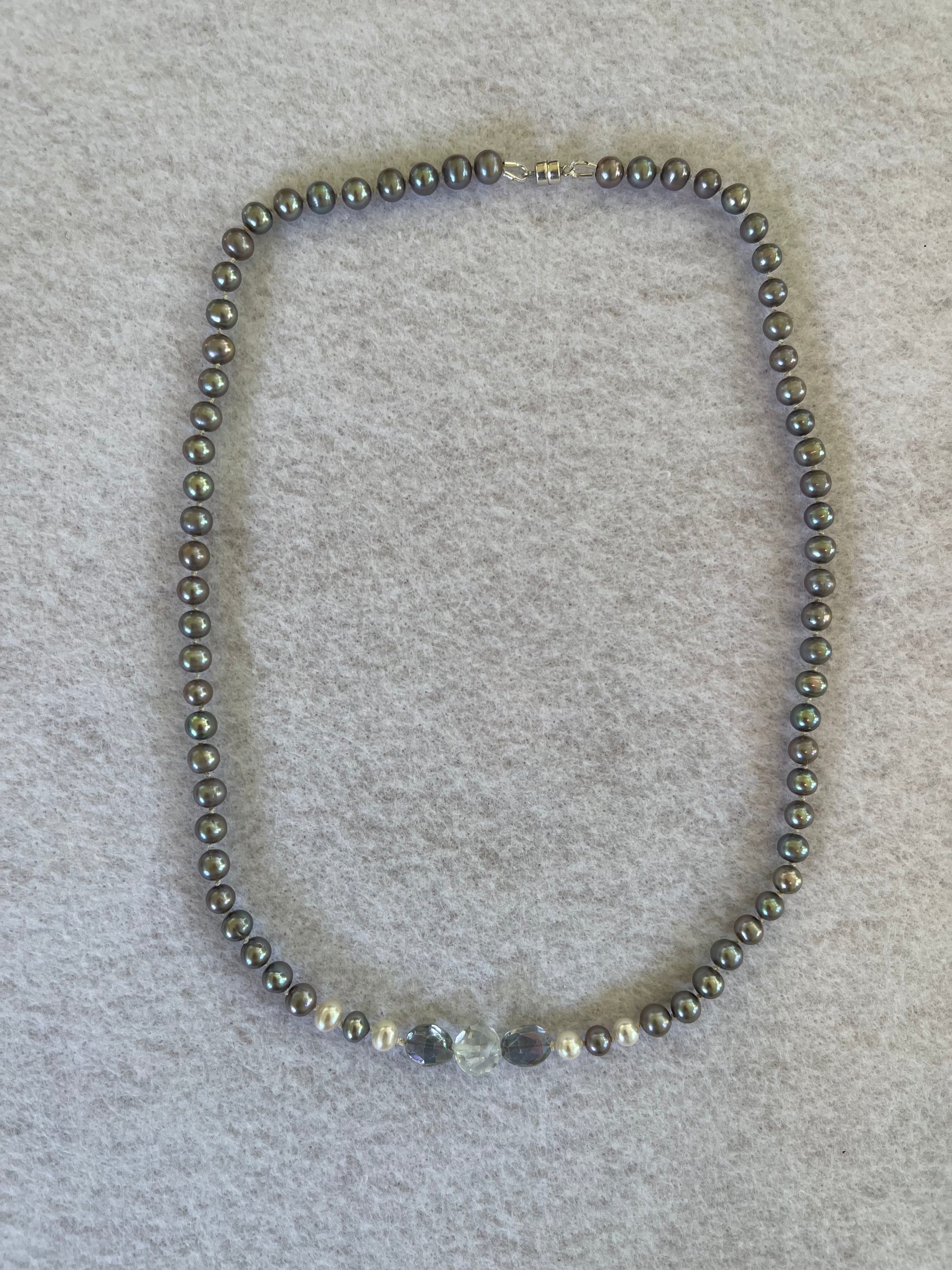 Necklace of Silver Peacock pearls with  Aquamarine and Rainbow Tourmaline focus beads on a white surface