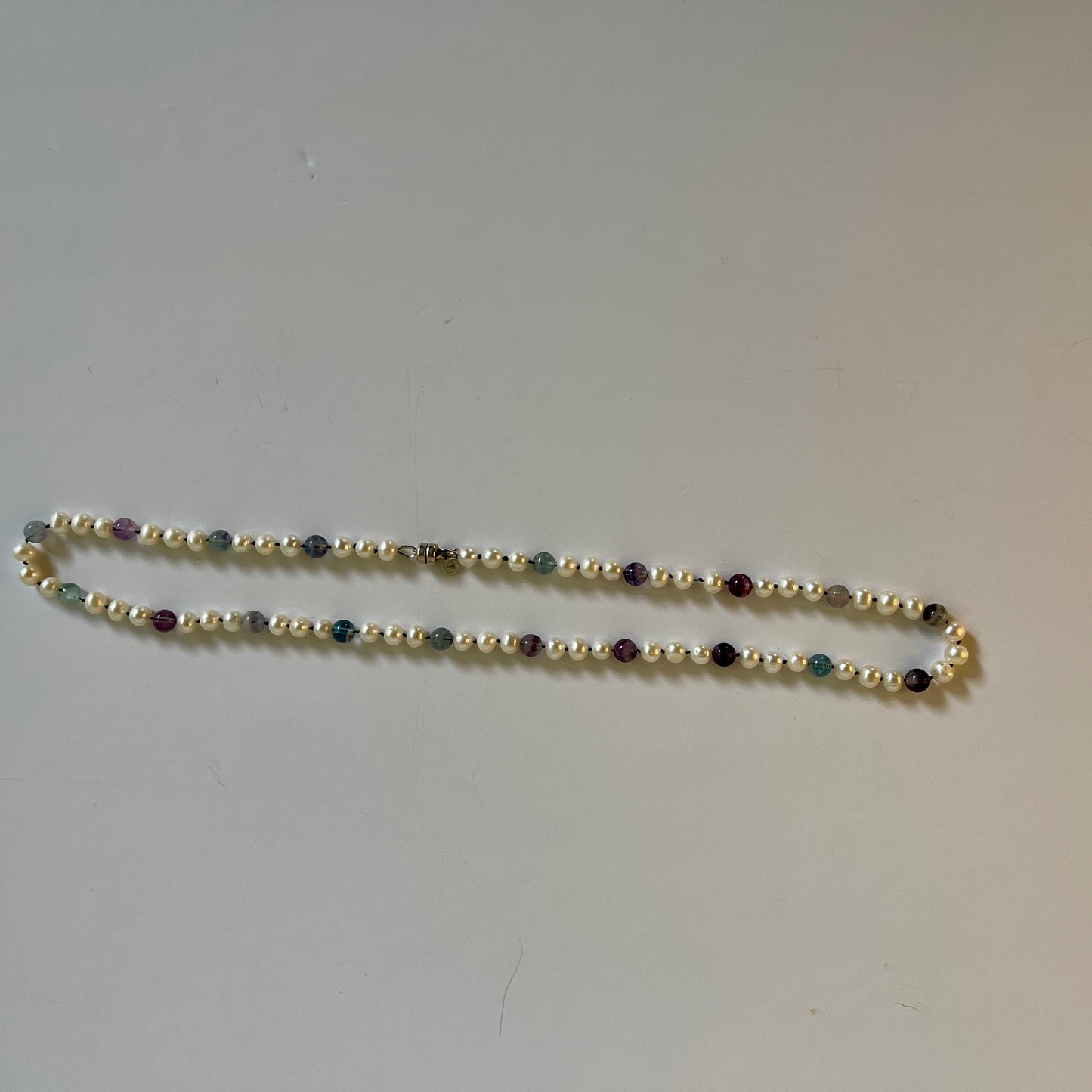 Beaded necklace with White Pearls and Fluorite beads on a plain background