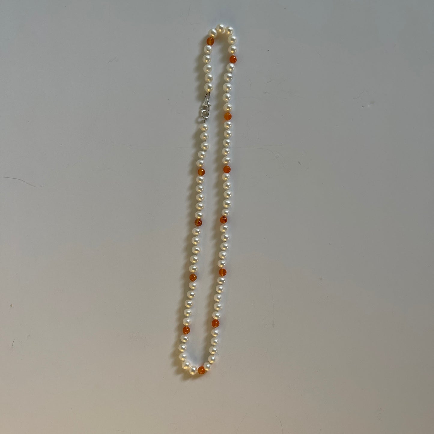 Pearl necklace with orange carnelian beads on a plain background