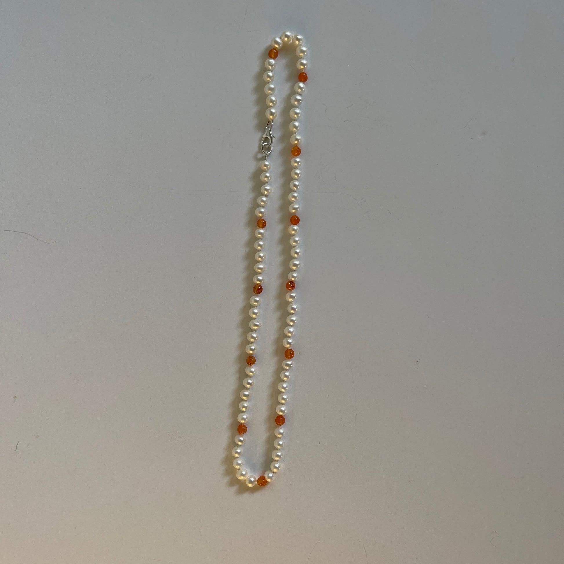 Pearl necklace with orange carnelian beads on a plain background