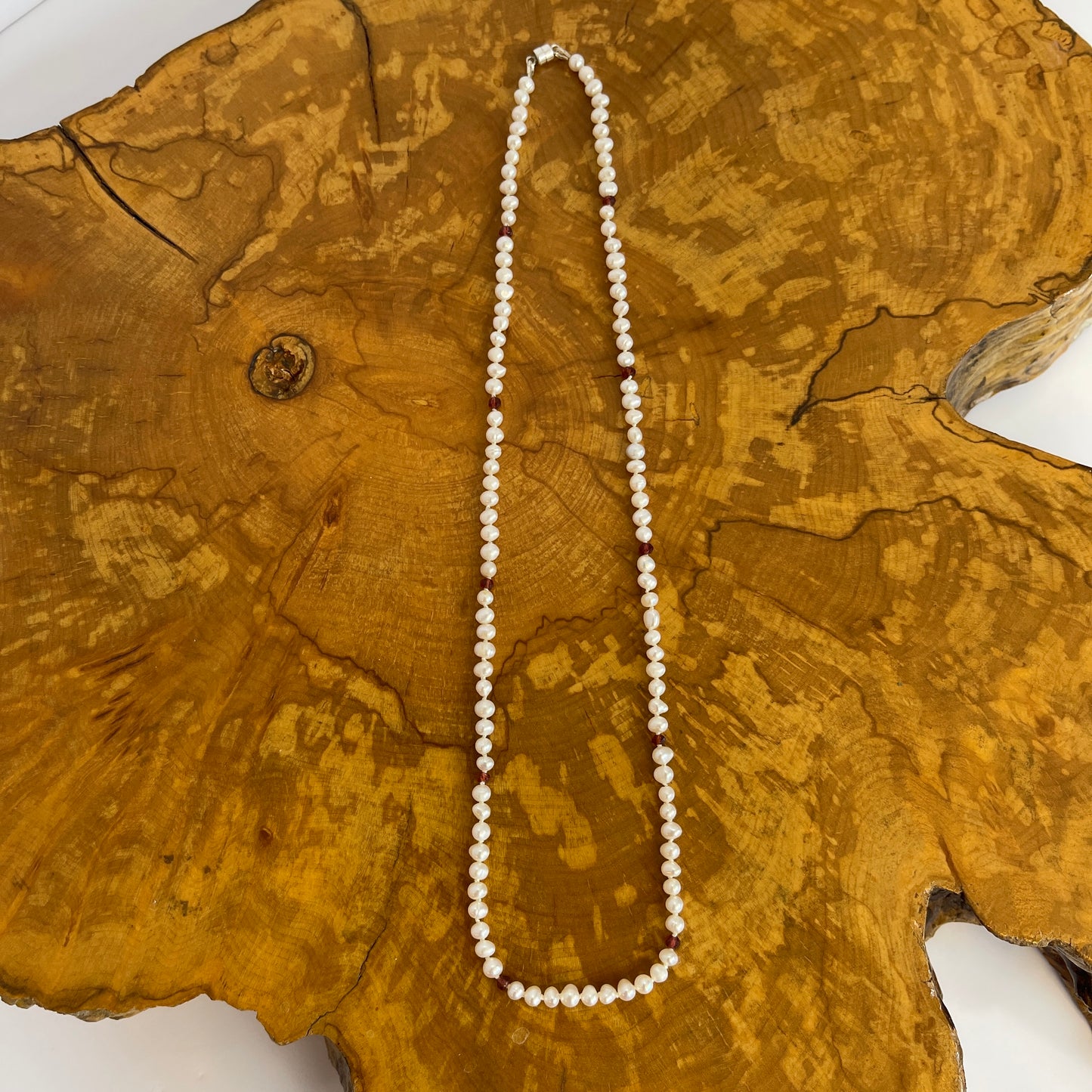 Pearl  and red cubic zirconia necklace on a wooden slab