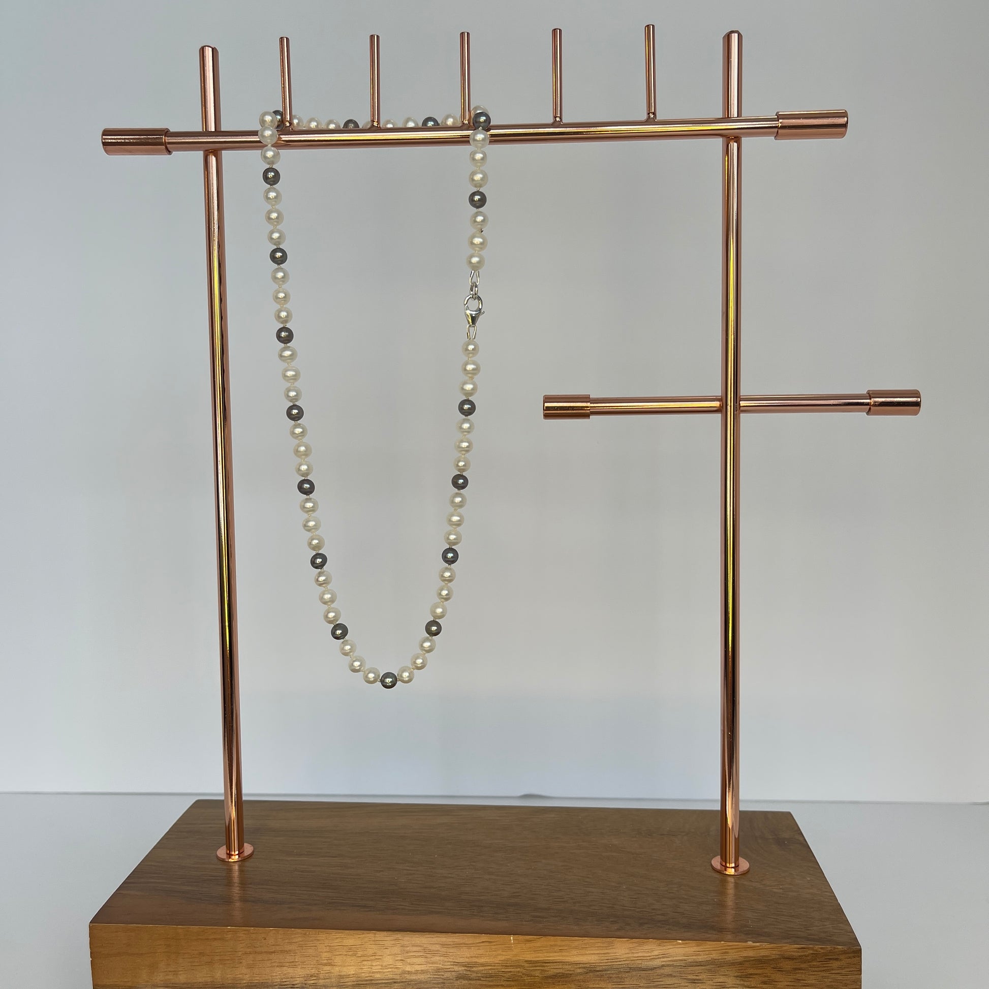 White and Silver Pearl necklace on a copper jewelry stand against a plain background