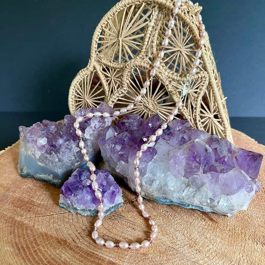 Necklace with Pink Pearls and purple cubic zirconia stones on a wooden surface with amethyst crystals and a woven decorative item.