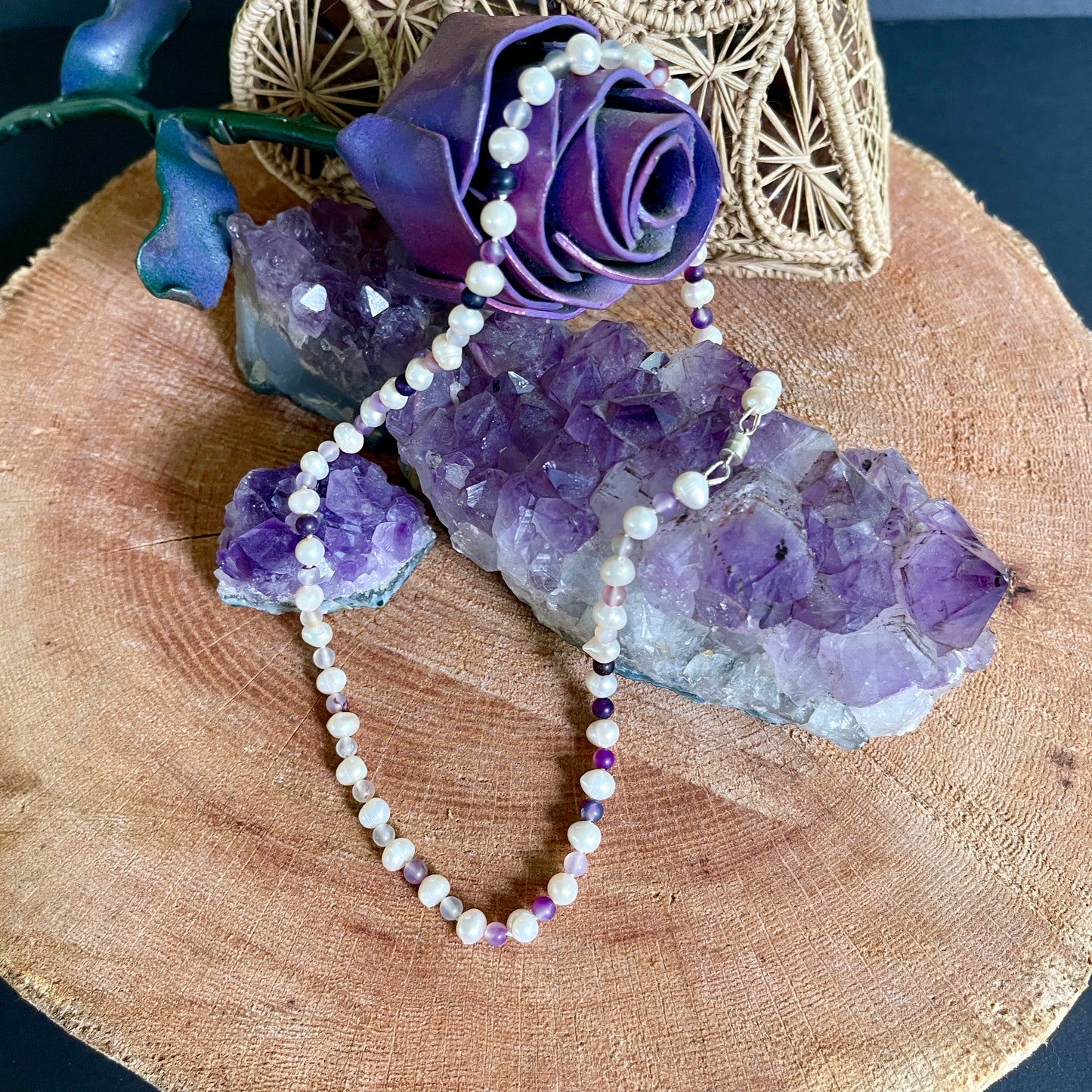 Necklace with purple and white beads on a wooden surface with amethyst crystals and a purple flower.