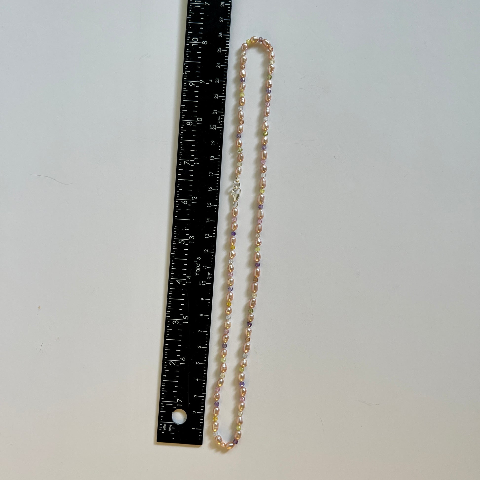 Necklace with mauve Pearls and multicolored cubic Ziconia stones on a wooden surface with amethyst crystal
Necklace next to a ruler on a white background
