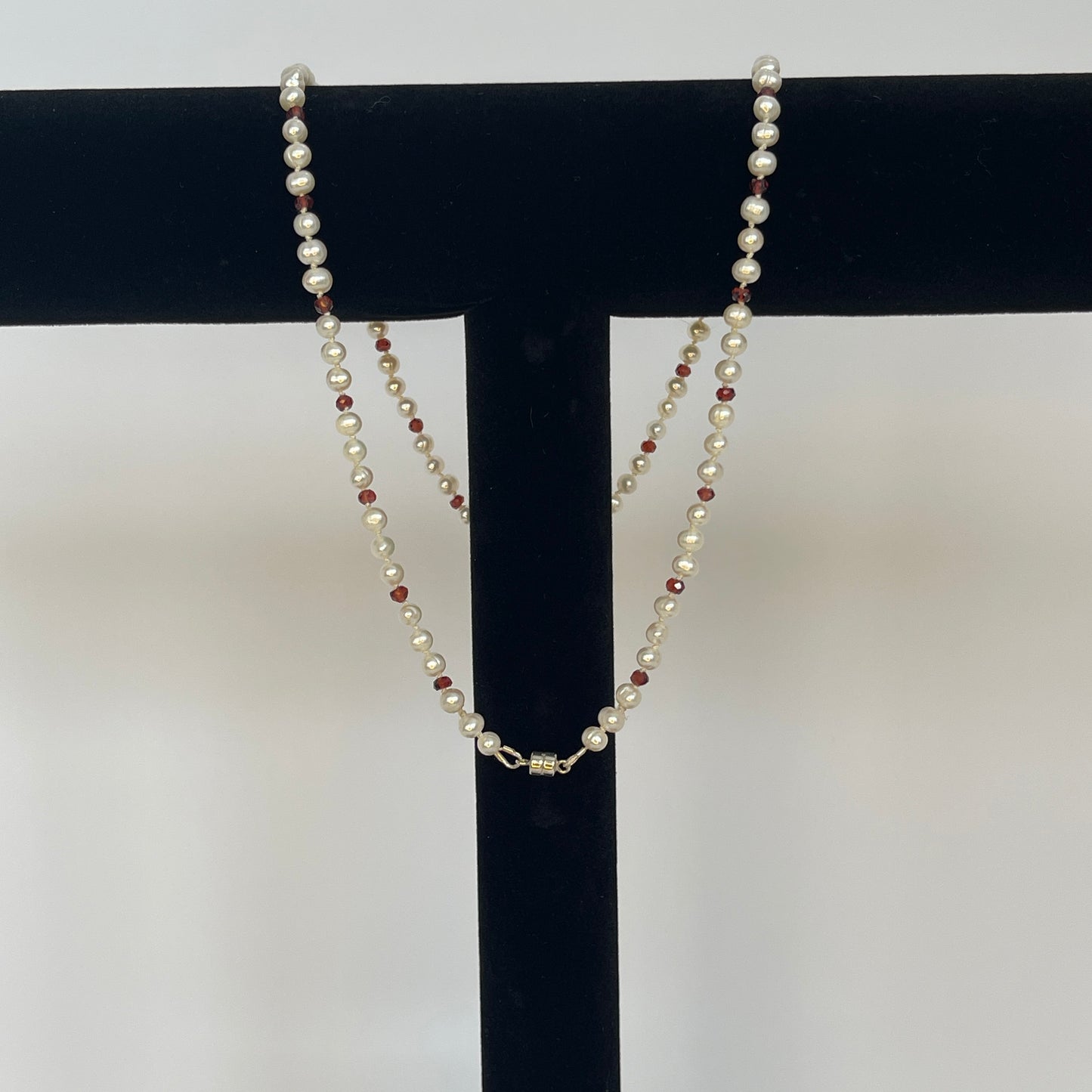 Necklace of White pearls and Garnet beads  and teardrops  showing magnet clasp on a black stand against a white background