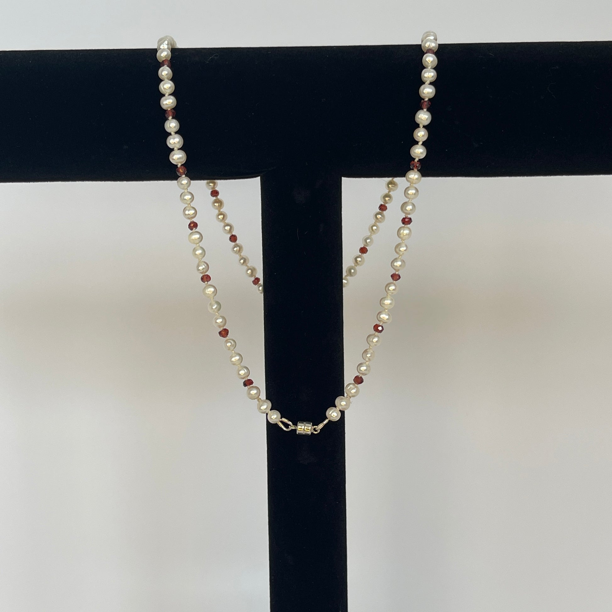 Necklace of White pearls and Garnet beads  and teardrops  showing magnet clasp on a black stand against a white background