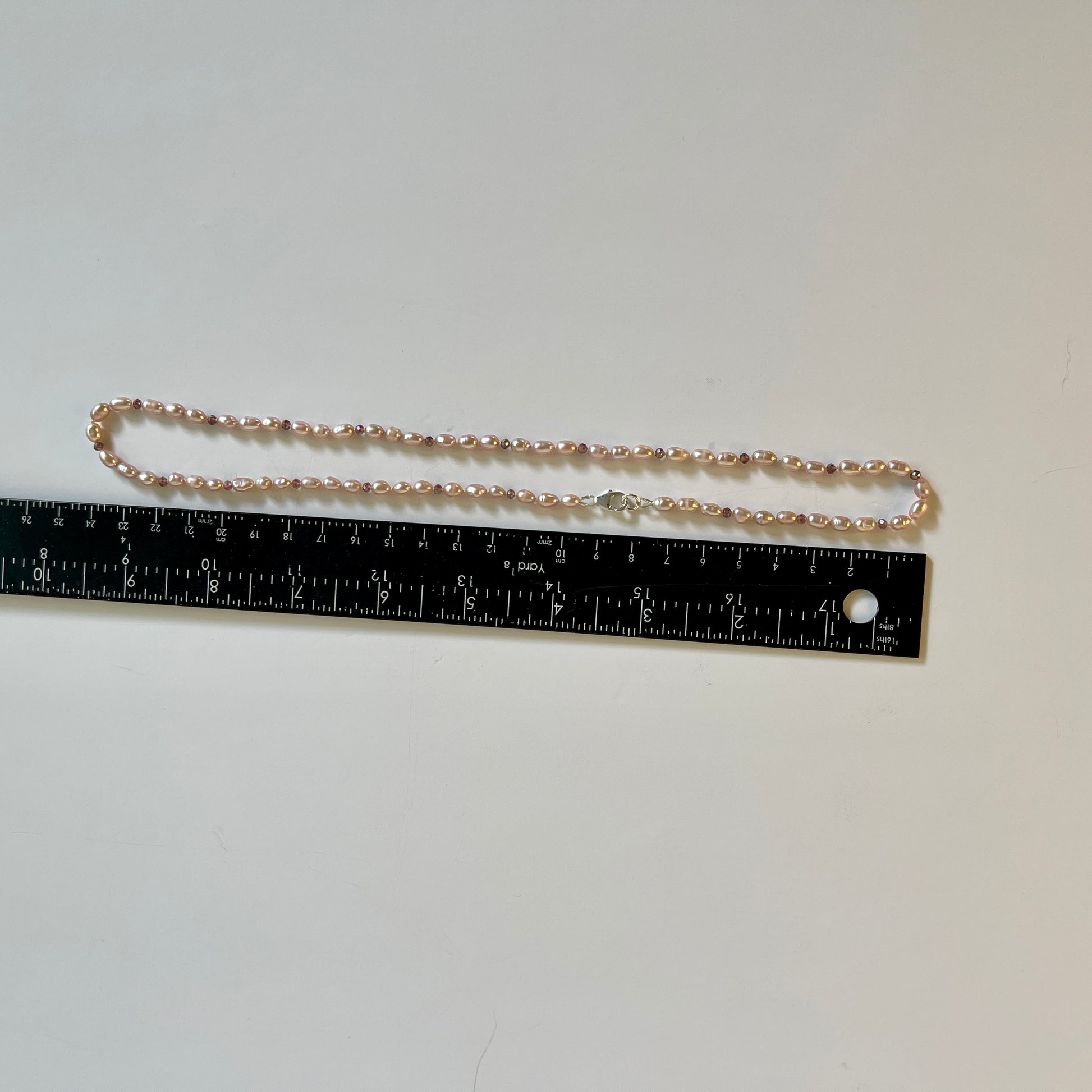 Pink pearls with cubic zirconia necklace next to a ruler on a white background