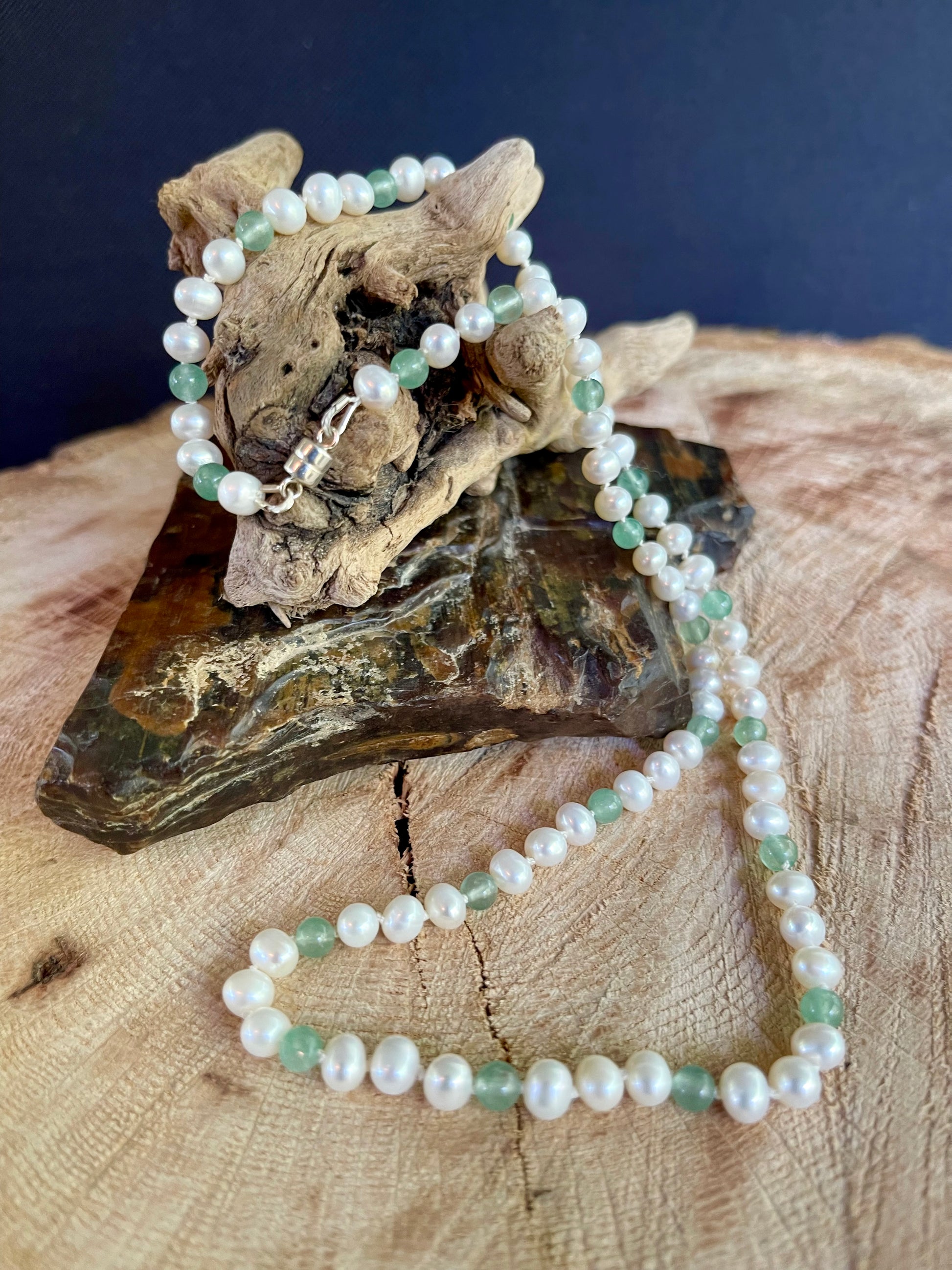 Pearl and Aventurine bead necklace draped over a piece of driftwood on a wooden surface with a dark background