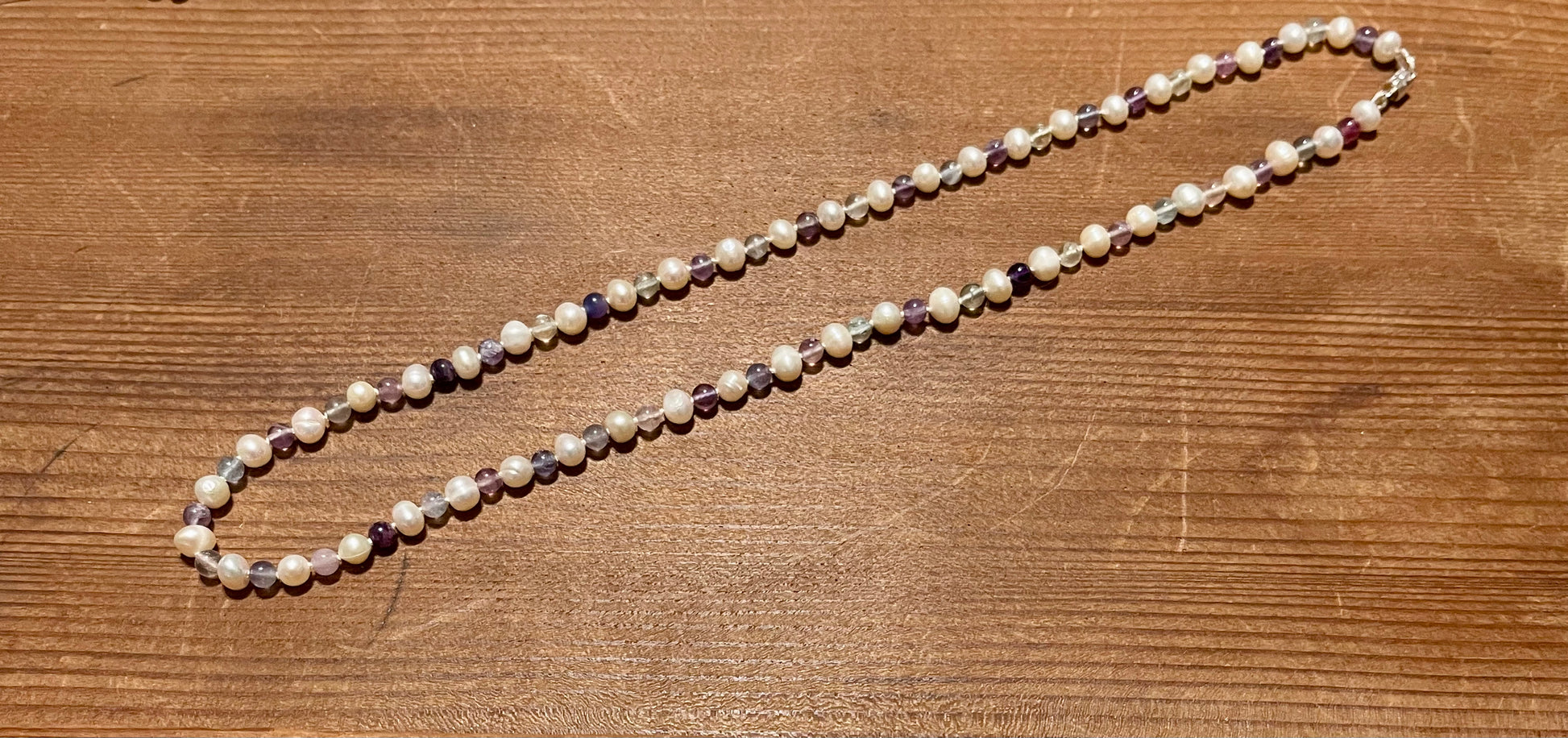 Necklace with purple Jasper and Pearl beads on a wooden surface 