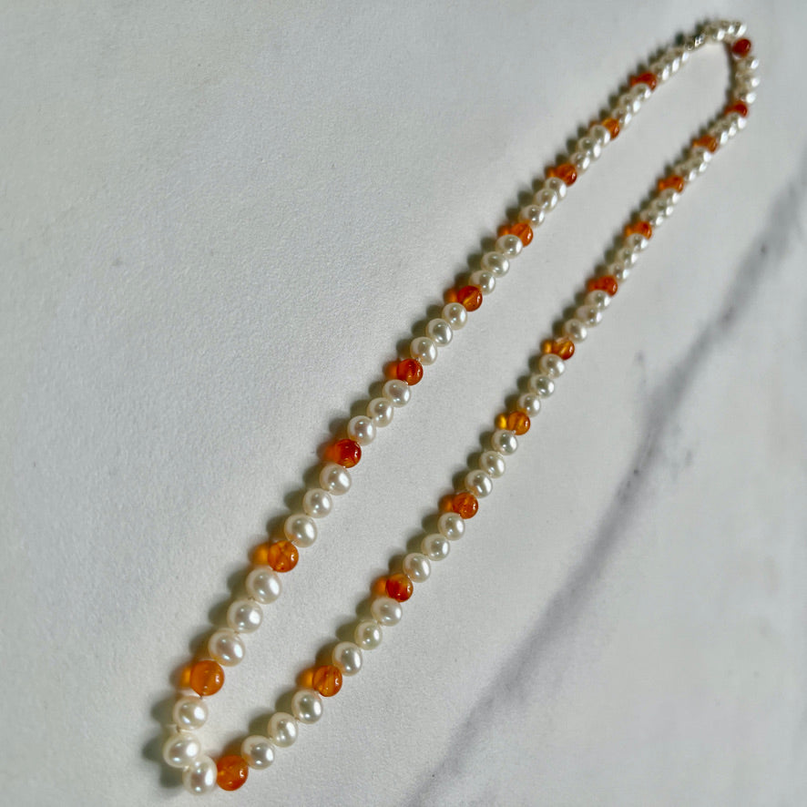 Necklace with white pearls and orange carnelian beads on a marble surface with natural elements
