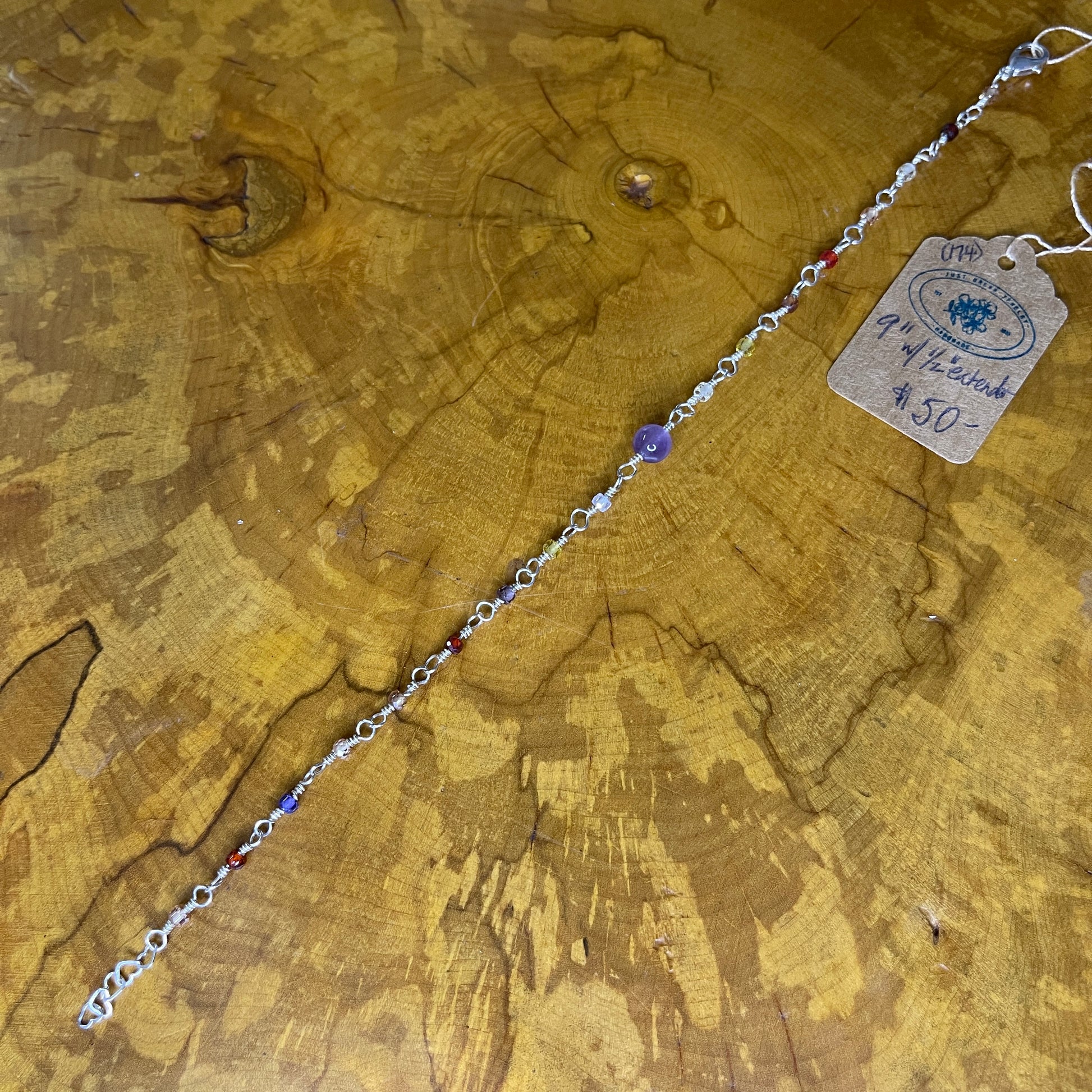 Multi colored Cubic Zirconia with Amethyst focus bead on Sterling Silver wire with Sterling Silver 1/2" heart chain  extender, 9" on wooden slab