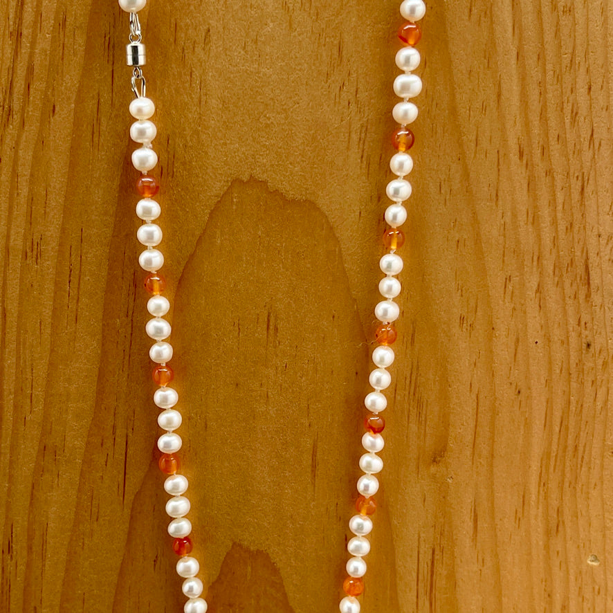 Necklace with white pearls and orange carnelian beads on a wooden surface 